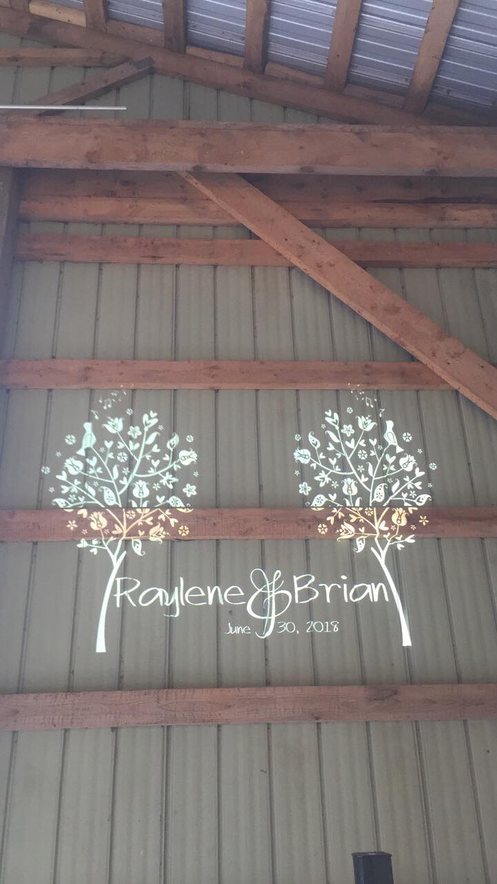 Tree-themed custom wedding monogram projected on a barn wall